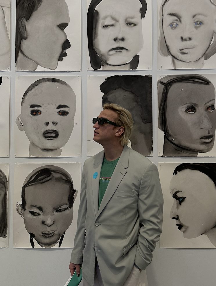 Mahir in a suit looking at a wall of painted portraits in a museum